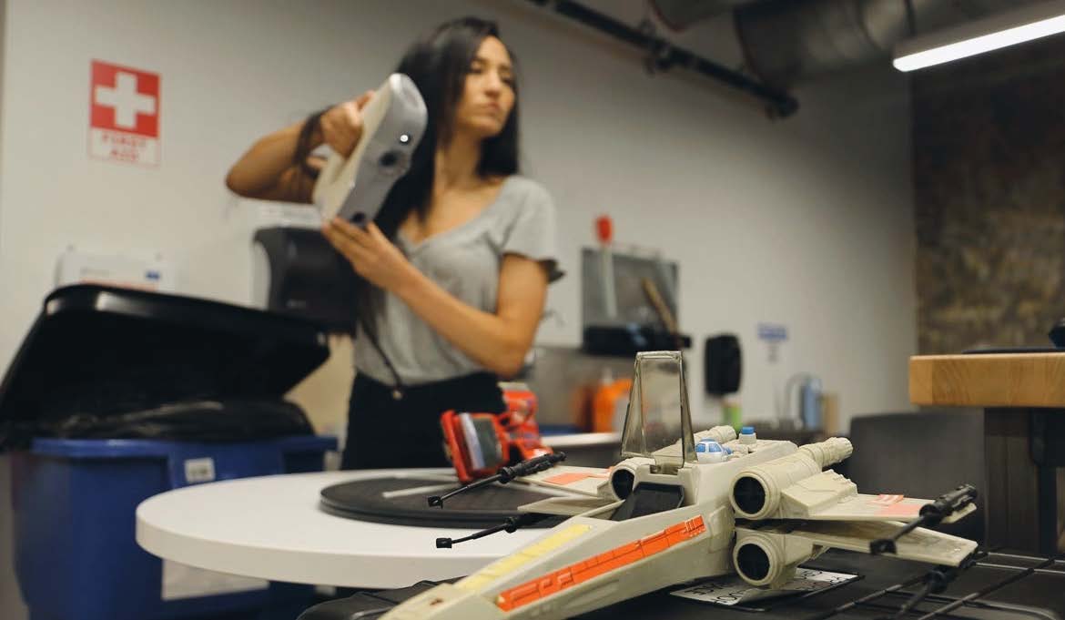 Annie Burke using a handheld 3D scanner, with a vintage X-wing toy on the work table.